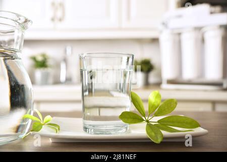 Bicchiere di acqua depurata con attrezzatura domestica e filtri su tavolo e cucina in background con attrezzatura per osmosi. Vista frontale. Co. Orizzontale Foto Stock