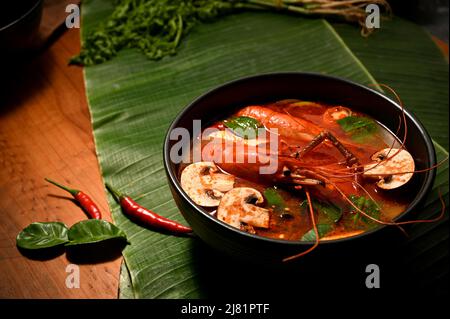 Tradizionale zuppa di cocco speziata thailandese con gamberi e ciotola di funghi su una foglia di banana. Tom Yum Kung Foto Stock