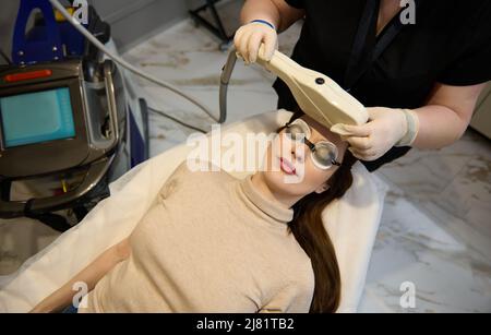 Bella donna caucasica che riceve il trattamento laser sul suo viso in clinica medica. Cura del viso. Rimozione dei capelli del laser facciale. Epilazione. Pelle liscia. Foto Stock