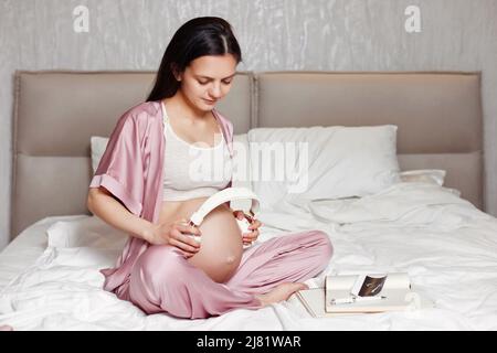 Donna incinta partecipazione delle cuffie sul suo ventre Foto Stock
