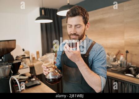 Bel barista con elegante caffè filtro profumato alla barba in caffetteria Foto Stock