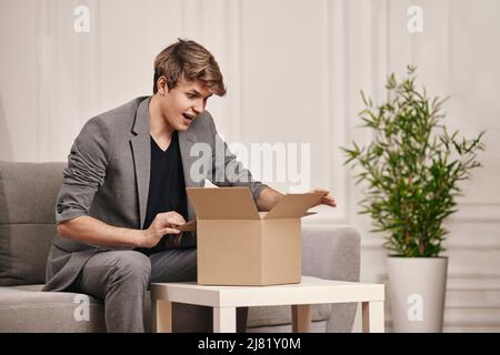 uomo seduto sul divano e disimballaggio scatola di cartone. Foto Stock