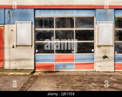 La stazione di servizio è chiusa ma mostra ancora porte blu e rosse sbiadite del garage. Foto Stock