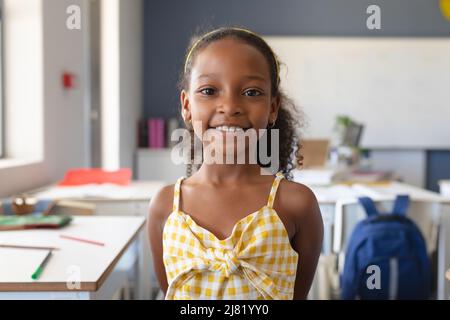 Ritratto di sorridente scolaretta elementare afroamericana in piedi in classe Foto Stock