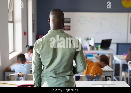 Vista posteriore del giovane insegnante maschile afroamericano in classe Foto Stock