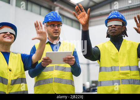 Ingegneri multietnici che utilizzano occhiali futuristici per realtà aumentata all'interno di una fabbrica robotica - concetto industriale e tecnologico - Focus sul volto dell'uomo centrale Foto Stock