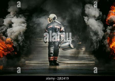Vigile del fuoco che indossa una tuta antincendio per la sicurezza sotto il caso di pericolo. Un vigile del fuoco cammina eroicamente tra il fumo nero e il fuoco mentre estinguono un rostro Foto Stock