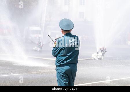 Un ufficiale del Ministero delle situazioni di emergenza della Russia si trova con la schiena contro lo sfondo di acqua corrente mentre estinguono un incendio. Foto Stock