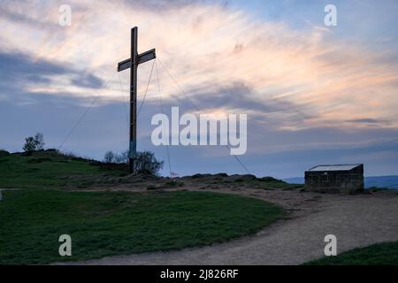 Alto torreggiante croce di Pasqua in legno (simbolo di speranza) tenuto con corde sulla cima della collina e rosso arancio tramonto cielo - il Chevin, Otley, West Yorkshire Inghilterra Regno Unito. Foto Stock