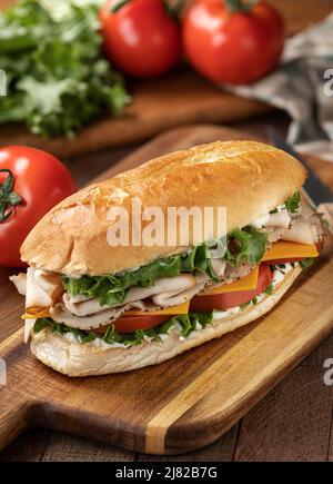 Sandwich sottomarino con tacchino, prosciutto, lattuga al formaggio e pomodoro su un rotolo di hoagie con lattuga e pomodori sullo sfondo Foto Stock