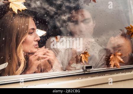 Giovane coppia di amanti felice dietro la finestra mistrata bagnato, pioggia drops.Drawing cuore con finger.Autumn atmosfera, umore, foglie di acero.Love romantico viaggio su strada. Foto Stock