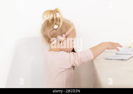 Bambino con impianto cocleare seduto a casa e mangiare. Ascolta il concetto di tecnologia innovativa di aiuto e medicina Foto Stock