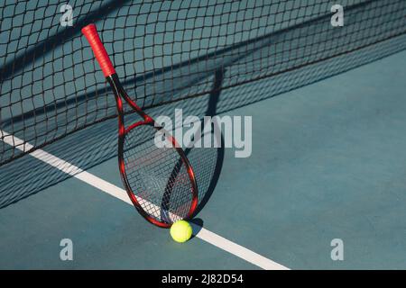 Vista ad alto angolo della racchetta rossa con palla appoggiata su rete al campo da tennis durante la giornata di sole Foto Stock