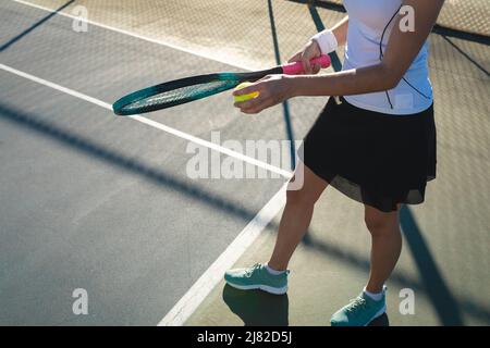 Bassa sezione di giovane donna caucasica che serve al campo da tennis in giornata di sole Foto Stock