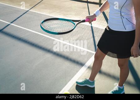 Bassa sezione di giovane donna caucasica che gioca al campo da tennis in giornata di sole Foto Stock