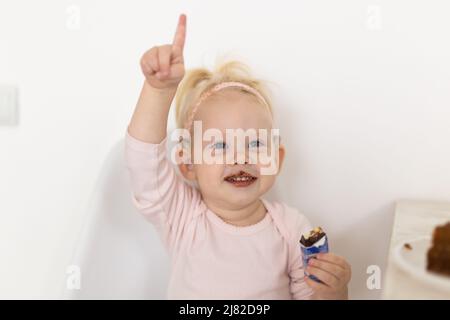 Bambino divertente con impianto cocleare seduta a casa e mangiare. Ascolta il concetto di tecnologia innovativa di aiuto e medicina Foto Stock