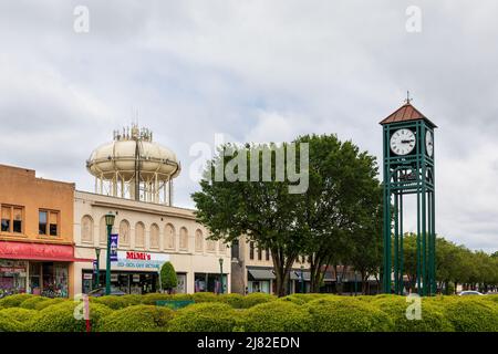 THOMASVILLE, NC, USA-8 MAGGIO 2022: Vista dell'orologio della città, della torre dell'acqua e del blocco di edifici di negozi d'epoca attraverso la linea di arbusti. Foto Stock