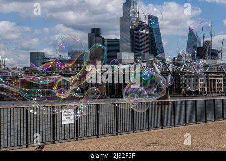 Londra UK, 12 maggio 2022. Un intrattenitore che crea bolle di sapone galleggianti di fronte allo skyline della città di londra e al quartiere finanziario. I timori di una recessione nel Regno Unito sono sempre più numerosi a causa dell’impatto di bollette energetiche più elevate e dei costi del carburante che riducono i redditi delle famiglie, come ha avvertito la Banca d’Inghilterra che il Regno Unito deve affrontare un forte rallentamento economico. Credit. amer Ghazzal/Alamy Live News Foto Stock