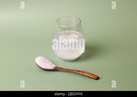 Polvere di collagene bianco in vetro trasparente con acqua e cucchiaio di legno su sfondo verde. Foto Stock