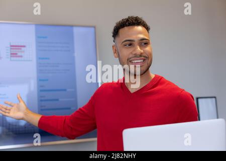 Sorridente uomo d'affari ispanico che dà la presentazione in sala riunioni durante la riunione sul posto di lavoro Foto Stock