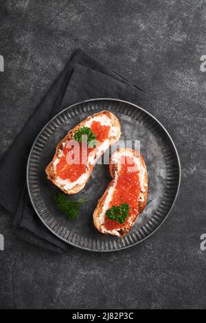 Due dandwiches con caviale rosso. Caviale rosso salmone in ciotola e sandwich server su vecchio piatto di ferro su sfondo vecchio tavolo nero. Vista dall'alto. Spazio di copia. Foto Stock