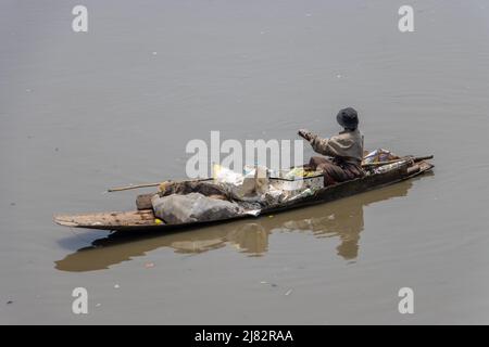 Un povero uomo galleggia su una vecchia barca piena di materiali riciclati Foto Stock