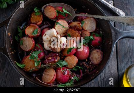 Padella il ravanello rosso fritto con cipolle, aglio e prezzemolo. Caramellato con sciroppo d'acero. Servito in una teglia in ghisa su sfondo di tavolo in legno. Foto Stock