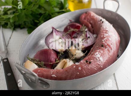 Filetto di maiale con cipolle rosse, erbe e aglio in una padella. Crudo e crudo. Pronto per cucinare Foto Stock