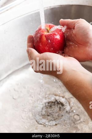 La mela rossa viene lavata nel lavandino Foto Stock