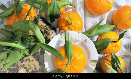 Clementine di tangerini freschi e maturi con foglie su tessuto bianco, vista dall'alto ancora vita, fuoco morbido Foto Stock