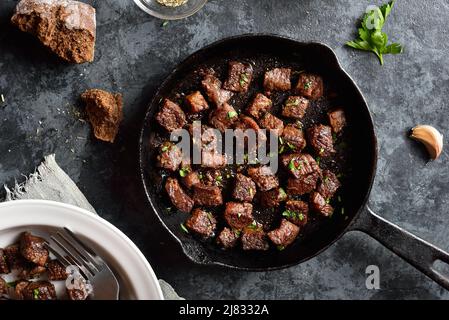Aglio burro bistecca morsi in padella su sfondo di pietra scura. Vista dall'alto, piatto Foto Stock