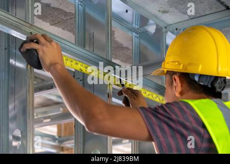 un operatore di costruzione esperto, che lavora come un cornamero sta misurando alcuni puntoni di supporto strutturale per aggiungere all'integrità strutturale del buidoutl Foto Stock