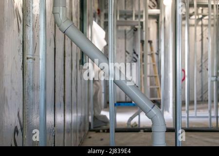 Un tubo in PVC grigio è integrato diagonalmente attraverso l'incorniciatura in acciaio galvanizzato dietro le pareti di un nuovo edificio Foto Stock