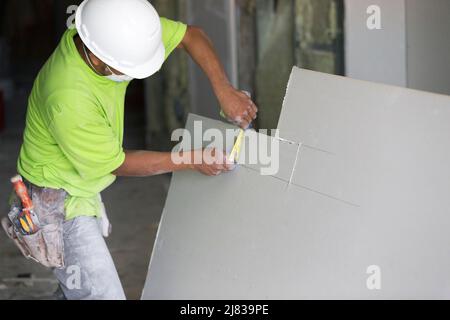 Operaio di costruzione - il gancio di Drywall taglia un pezzo di drywall o di sheetrock alle specifiche per allora essere appeso su acciaio galvanizzato che incornicia Foto Stock