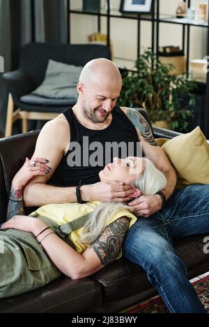 Scatto verticale di uomo e donna maturi in amore trascorrere il tempo insieme a casa rilassarsi sul divano in salotto Foto Stock