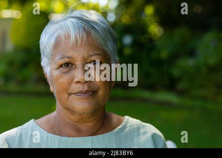 Primo piano ritratto di fidata donna anziana biraciale con corti capelli grigi contro le piante nel parco Foto Stock