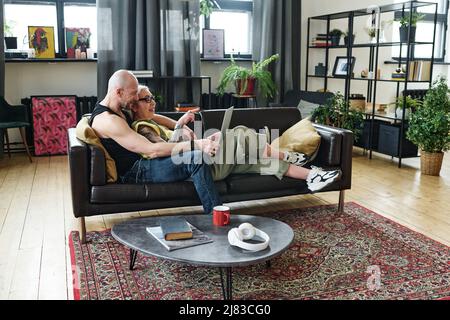 Uomo e donna caucasica matura in amore rilassarsi sul divano in soggiorno a casa guardando video in Internet su un portatile Foto Stock
