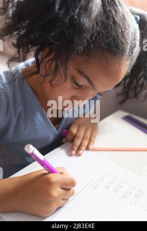 Primo piano della studentessa biraciale elementare che risolve le somme di matematica sul libro alla scrivania in classe Foto Stock