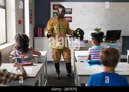 Giovane insegnante maschile afroamericano in vigile del fuoco uniforme insegnamento studenti elementari multirazziale Foto Stock