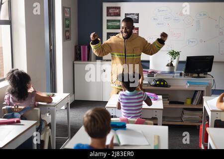Giovane insegnante africano americano di sesso maschile in uniforme vigile del fuoco con studenti elementari multirazziali Foto Stock