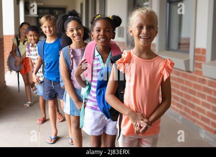 Ritratto di sorridenti studenti della scuola elementare multirazziale con zaino in fila a scuola Foto Stock