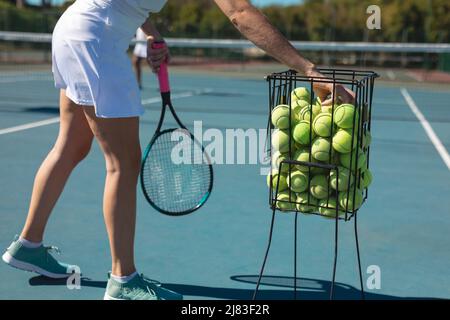 Bassa sezione di giovane donna caucasica che pratica il tennis in campo in giornata di sole Foto Stock