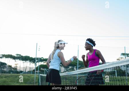 Felice multirazziale giovani donne giocatori che danno pugno su rete al campo da tennis Foto Stock