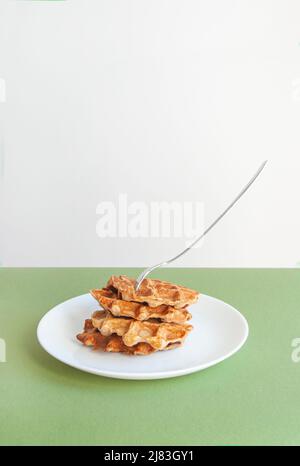 I waffle belgi fatti in casa si accatastano con la forchetta al centro su un tavolo di colore verde. Foto Stock