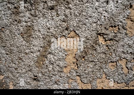 Una parete molto fragile, dove l'intonaco si sta sgretolando e ottiene un aspetto molto metallico quando il sole lo colpisce. Foto Stock