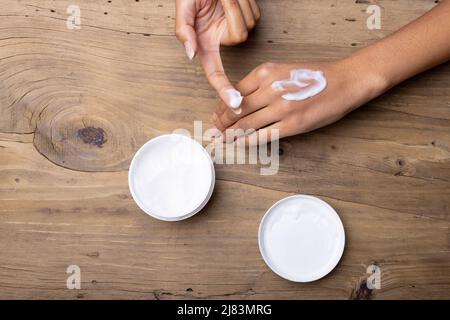 Mani croppate di afroamericana metà adulta donna applicazione unguento su nocche su tavola di legno Foto Stock