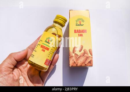 Mani che tengono in mano l'olio di mandorle pure Dabur o la confezione di bottiglie di Badam in confezione gialla isolata su sfondo bianco Foto Stock