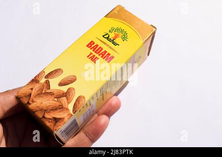 Mani che tengono in mano l'olio di mandorle pure Dabur o la confezione di bottiglie di Badam in confezione gialla isolata su sfondo bianco Foto Stock