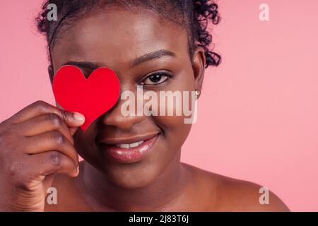 pelle scura signora che mostra due carta carta forma cuore figura forma bella data invito isolato rosa studio sfondo, invio di airkiss Foto Stock