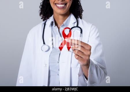 Metà sezione di sorridente medico afroamericano medio adulto femmina tenendo rosso Aids nastro di consapevolezza Foto Stock